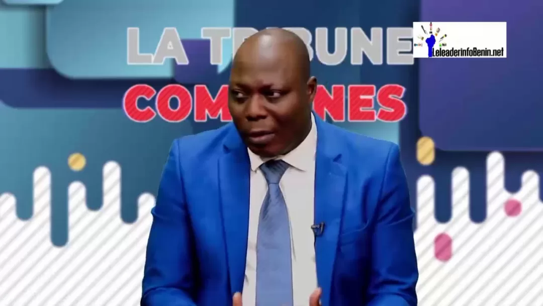 Homme en costume bleu parle dans un studio avec un panneau "LA TRIBUNE DES COMMUNES" en arrière-plan