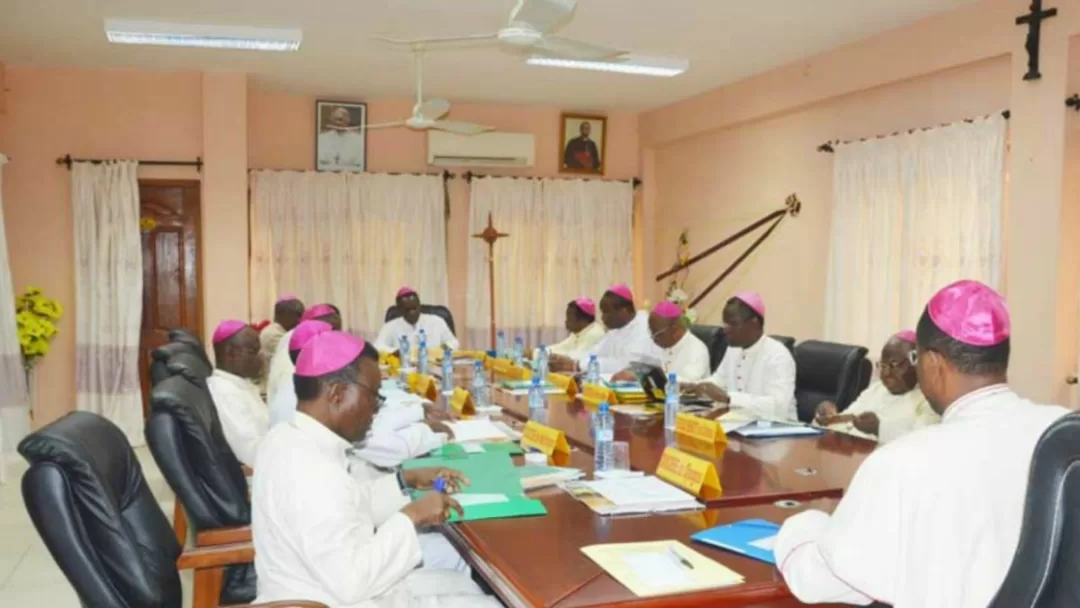 Un groupe de religieux en soutanes blanches et coiffés de zucchettos violets assis autour d'une grande table lors d'une réunion.