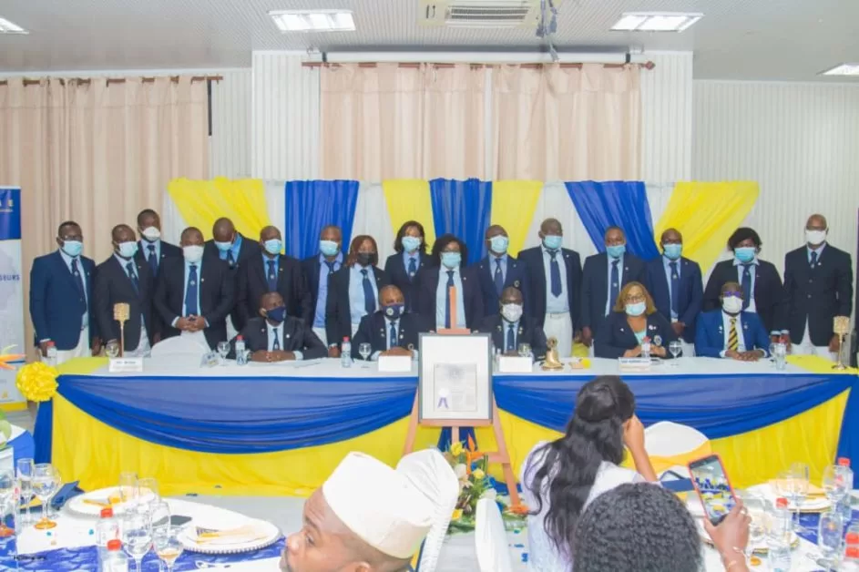 Un groupe de personnes en costume et masques pose derrière une table drapée de jaune et bleu lors d'une cérémonie officielle