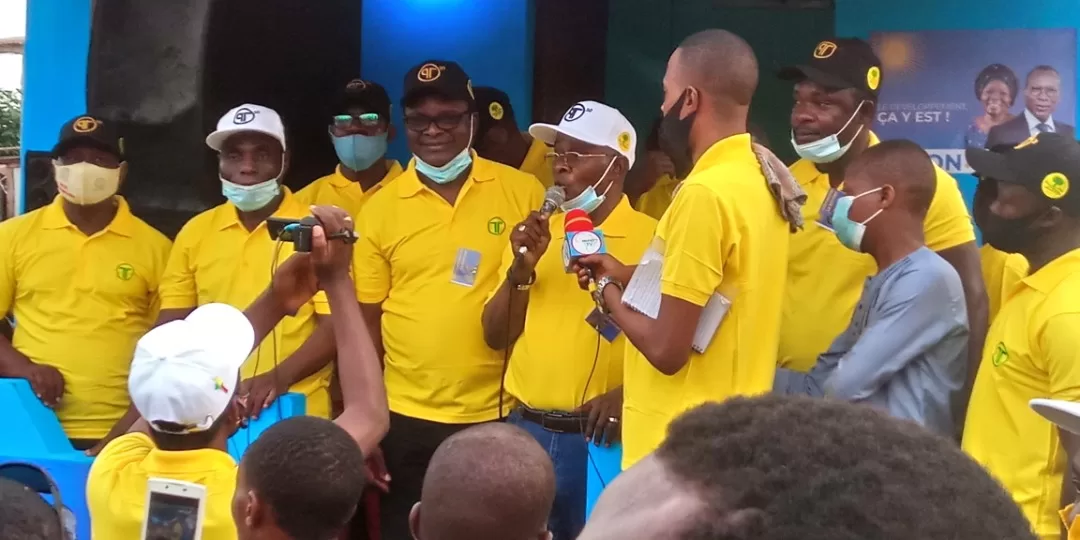Plusieurs hommes en polo jaune et casquette, certains masqués, s’adressent à un petit groupe au cours d’un rassemblement public