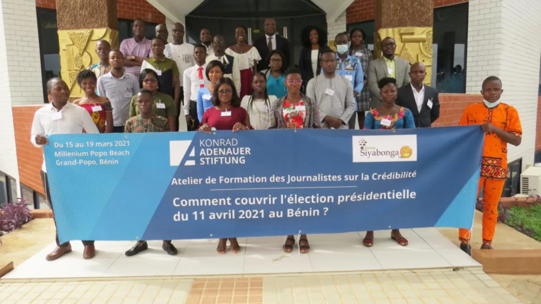 Groupe de personnes posant devant un bâtiment avec une grande bannière bleue sur la couverture d'une élection présidentielle