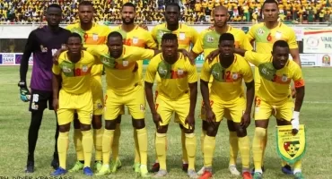 Onze joueurs de football posant en tenue jaune sur un terrain avant un match devant des tribunes remplies de spectateurs