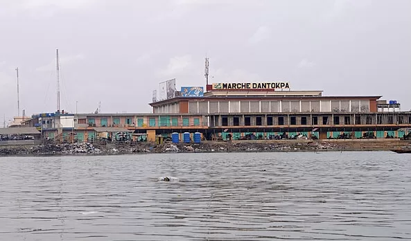 grand bâtiment long vu de loin avec panneau marché dantokpa face à un plan d'eau calme sous un ciel nuageux