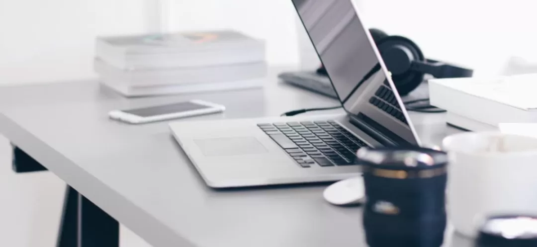 Bureau avec ordinateur portable ouvert, smartphone, tasse et piles de documents sur une table claire