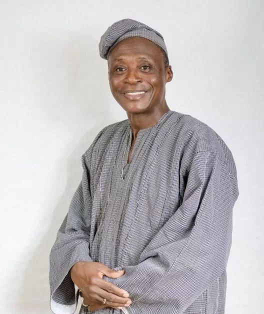 Homme souriant vêtu d’une tenue traditionnelle à carreaux et coiffé d’un bonnet assorti sur un fond clair