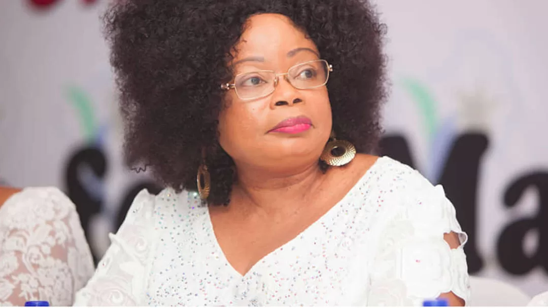 Femme portant une blouse blanche à motifs dentelle et coiffure afro regardant vers la droite avec un fond flou