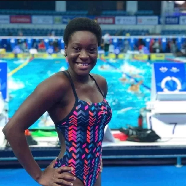 Jeune nageuse souriante en maillot de bain coloré posant devant un bassin de natation en intérieur