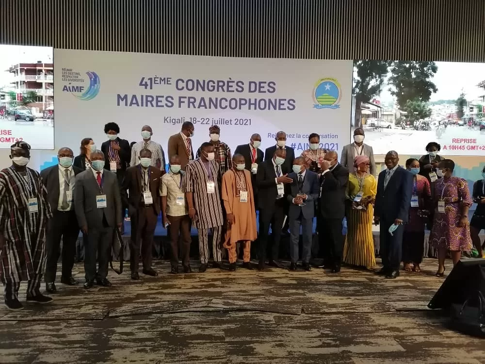 Groupe de personnes posant devant un panneau avec texte «41ème congrès des Maires Francophones» avec masques et badges d’identification