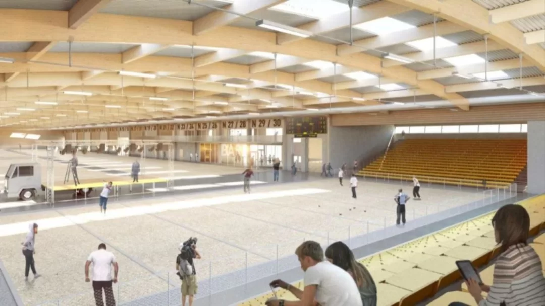 Intérieur d’un boulodrome avec terrain de pétanque, gradins jaunes et plusieurs personnes en activité et spectateurs assis