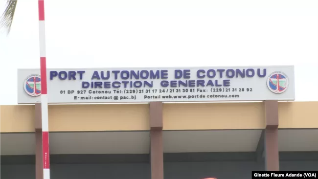 Panneau du Port Autonome de Cotonou avec coordonnées affichées sur un bâtiment beige et poteau rouge et blanc devant