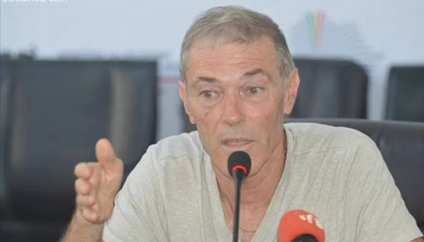 Un homme parle en gesticulant devant un micro rouge lors d’une conférence de presse