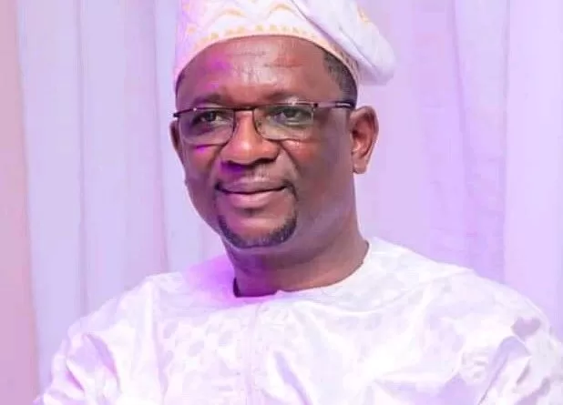 Homme souriant portant une tenue traditionnelle blanche et un bonnet assorti sur un fond blanc.