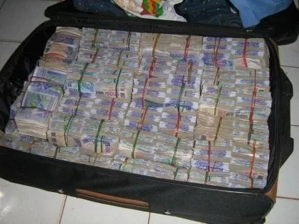 Valise ouverte contenant de nombreuses liasse de billets de banque empilés et attachés par des élastiques colorés