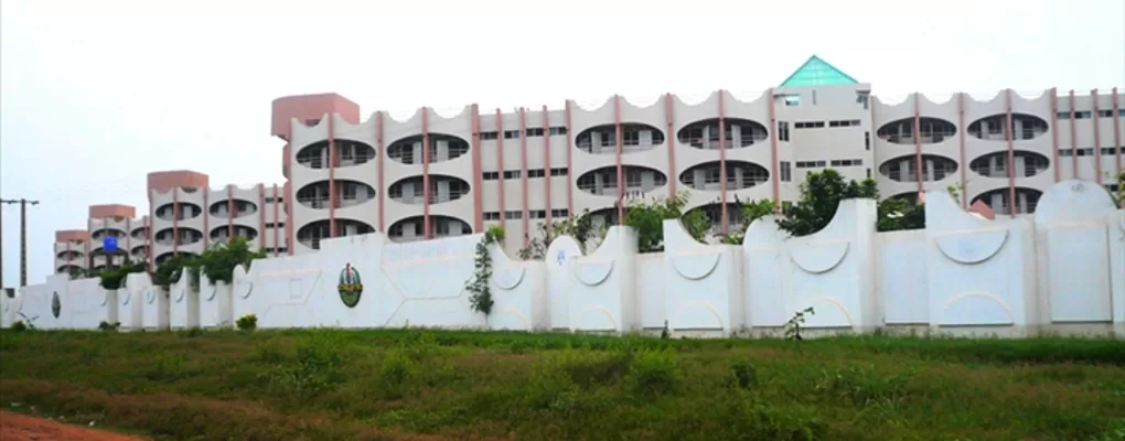 Grand bâtiment moderne derrière un mur blanc orné de motifs et de végétation devant un terrain herbeux