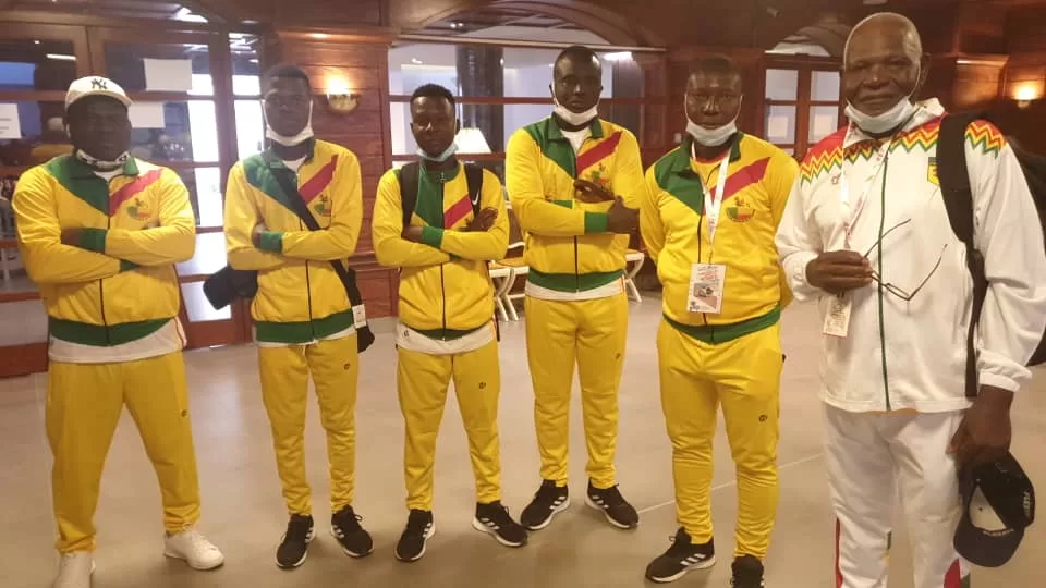 Six hommes portant des survêtements jaunes et un homme en tenue blanche posent dans un intérieur lumineux
