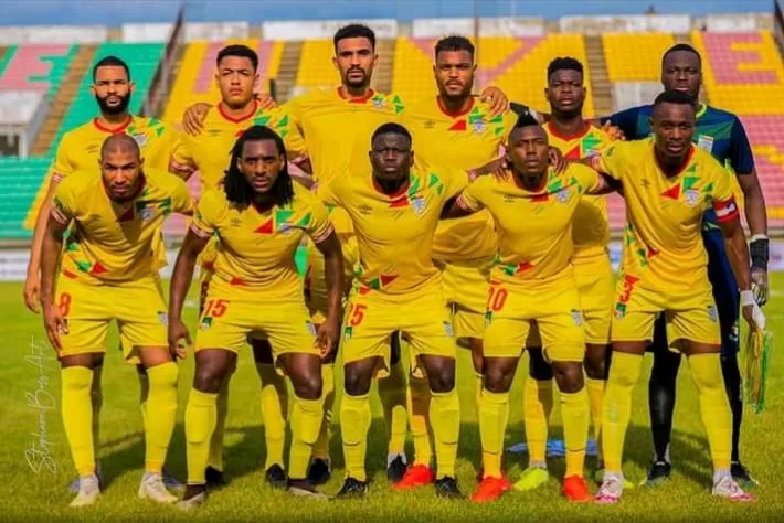Onze joueurs en tenue sportive jaune posent ensemble sur un terrain de football dans un stade avec des gradins vides en arrière-plan