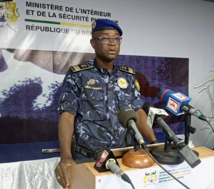 Un officier de police en uniforme bleu marine casque bleu parle devant plusieurs microphones lors d’une conférence de presse
