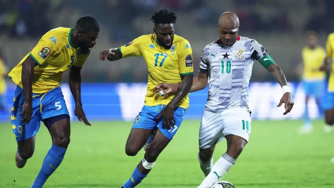 Trois joueurs de football en action sur un terrain, deux en maillots jaunes et un en maillot blanc contrôlant le ballon