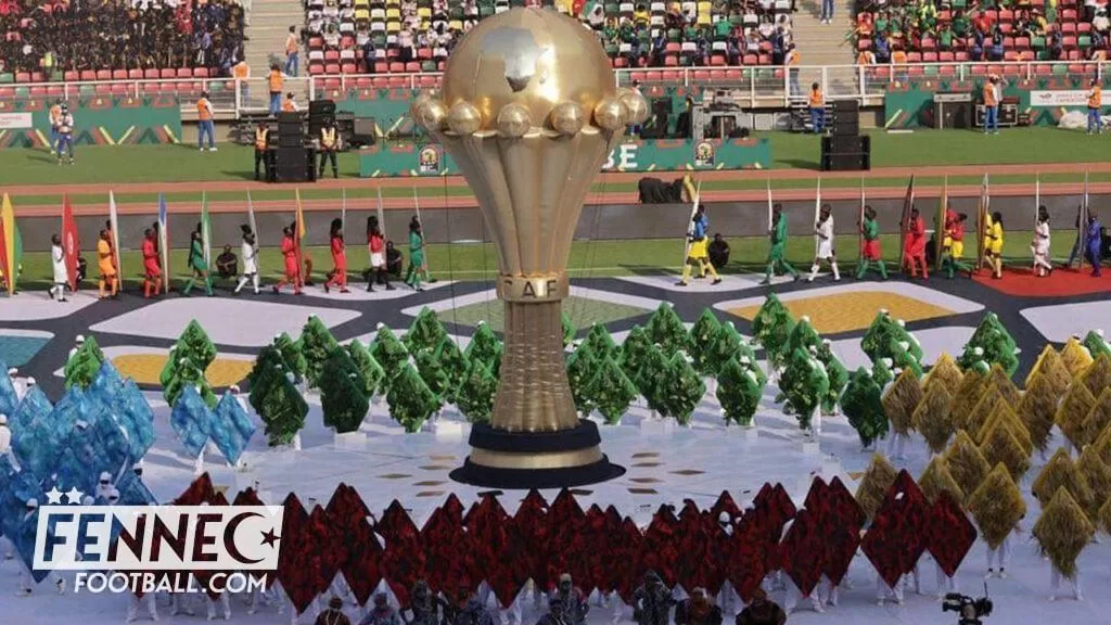 Grande coupe dorée au centre d'un stade avec des danseurs en costumes colorés alignés autour et spectateurs en tribunes