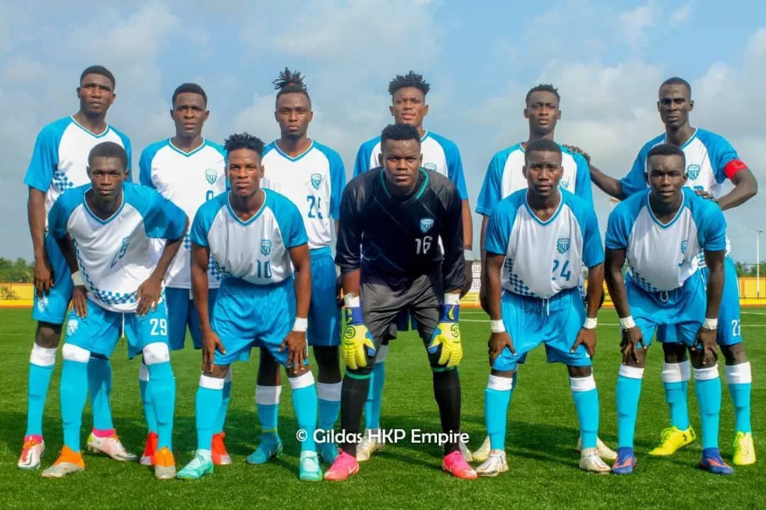 Onze joueurs de football en tenue bleue et blanche posant en formation sur un terrain herbeux sous un ciel partiellement nuageux