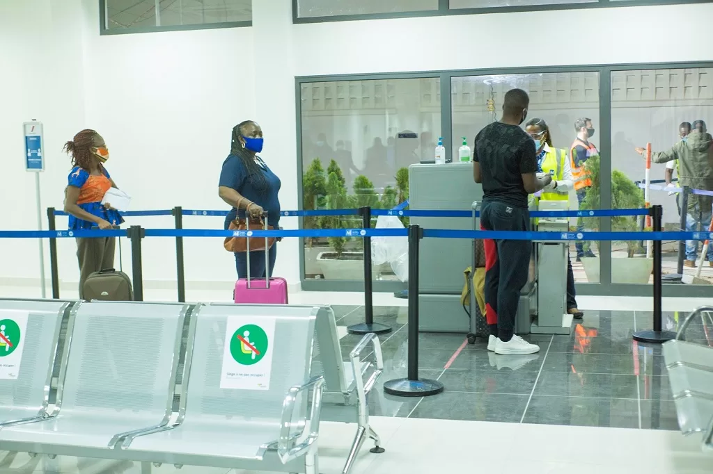 Des passagers en file d attente au contrôle de sécurité dans un hall d aéroport avec des agents en tenue et masques sanitaires