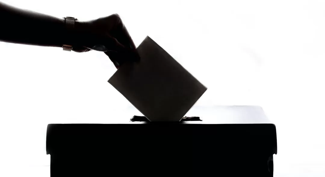 Main déposant un bulletin dans une urne de vote devant un fond blanc lumineux