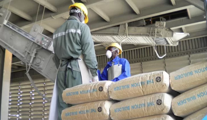 Deux ouvriers en tenue de protection discutent dans une usine avec des sacs de ciment empilés au premier plan