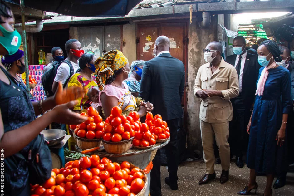 Un groupe de personnes masquées visite un marché avec des paniers de tomates et des produits alimentaires visibles