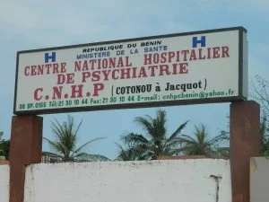 Panneau d’entrée d’un centre national hospitalier de psychiatrie face à un ciel bleu avec trois palmiers derrière un mur blanc