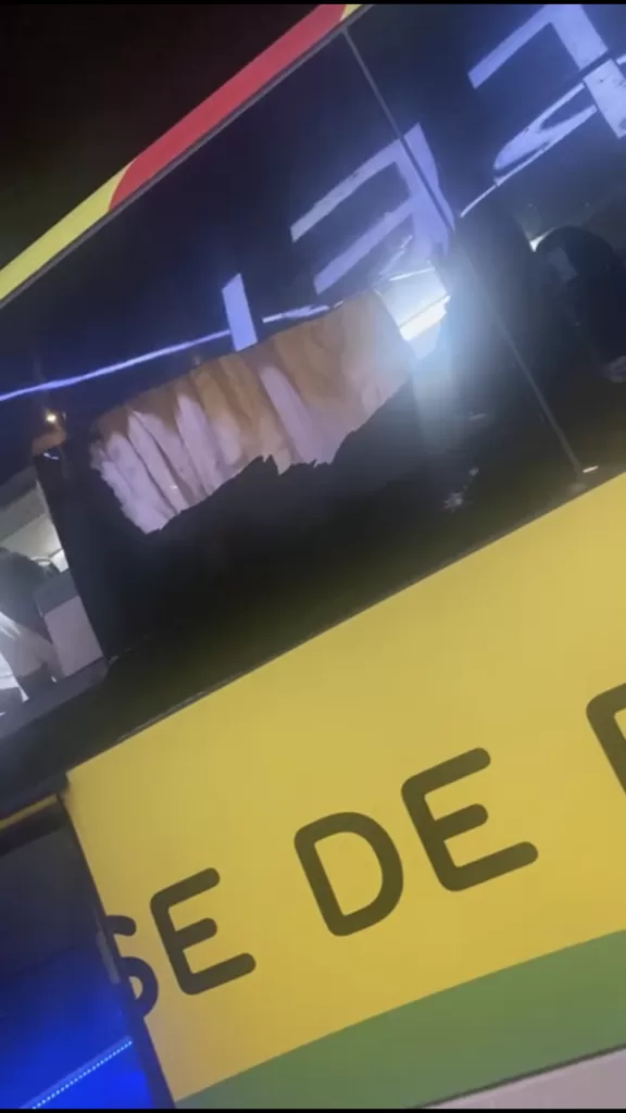 Fenêtre latérale d’un bus de couleur jaune endommagée avec un grand trou dans la vitre en plein soir