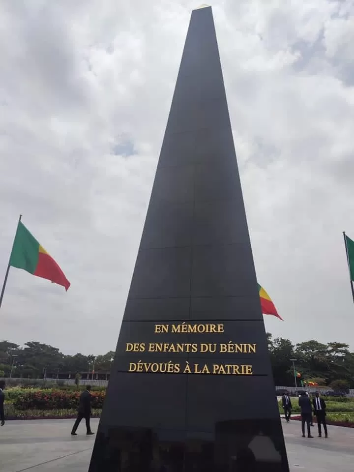 Obélisque noir avec inscription dorée en mémoire des enfants dévoués entouré de drapeaux colorés et de personnes au sol