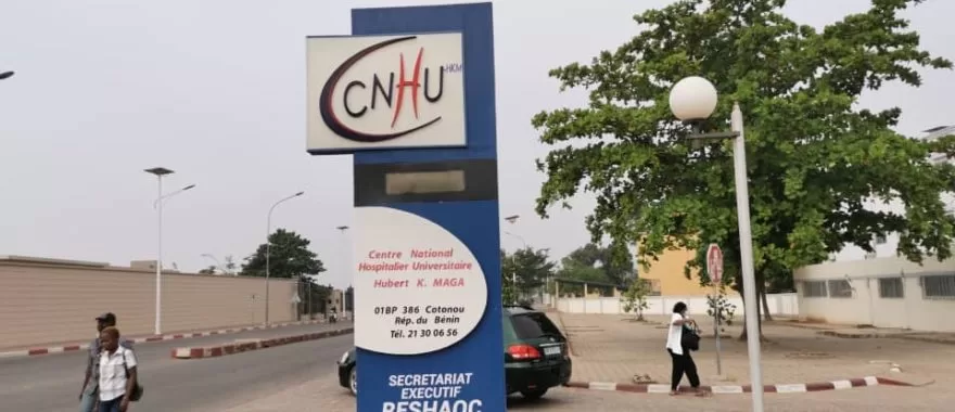Totem indiquant le Centre National Hospitalier Universitaire avec personnes marchant autour et une voiture garée à proximité