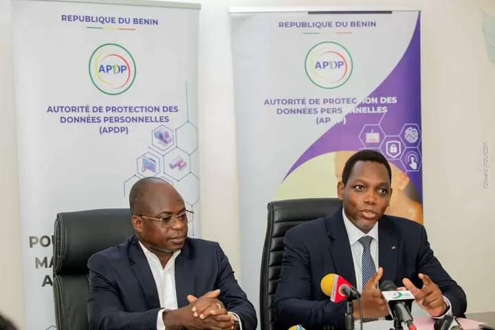 Deux hommes en costume parlent lors d’une conférence avec des panneaux officiels sur la protection des données personnelles en arrière-plan