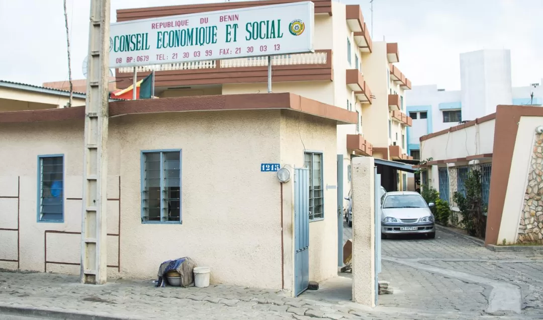 Entrée d'un bâtiment administratif avec un panneau « Conseil économique et social » et une voiture stationnée sur un chemin adjacent