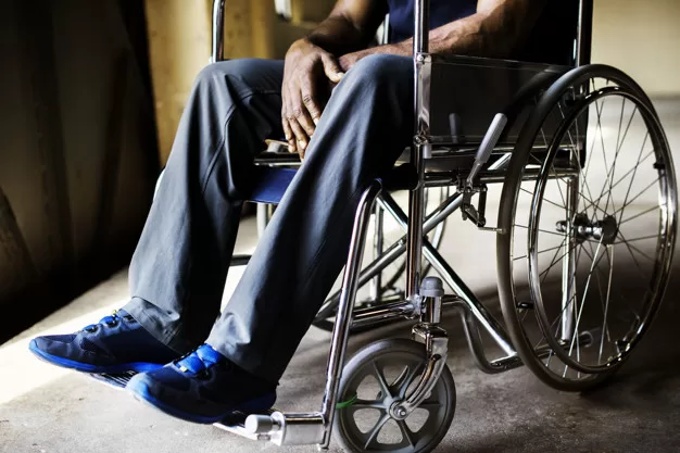 Personne assise dans un fauteuil roulant avec des chaussures bleues et un pantalon gris dans un intérieur sombre