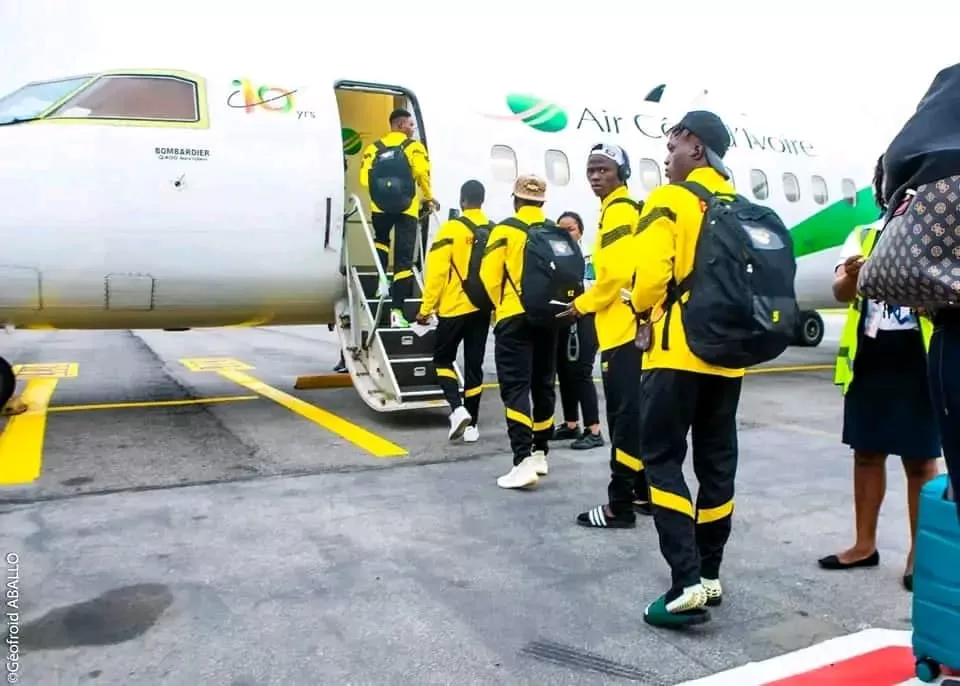 Des jeunes hommes en tenue jaune et noire montent dans un avion blanc marqué Air Caraïbes sur le tarmac