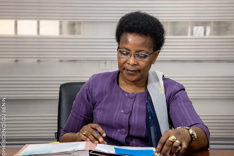 Femme portant des lunettes et un vêtement violet consulte des documents posés sur un bureau dans un bureau moderne