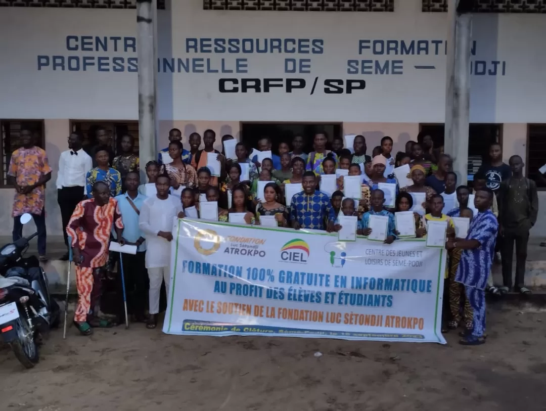Groupe de jeunes et adultes posant devant un bâtiment avec une grande banderole de formation gratuite en informatique