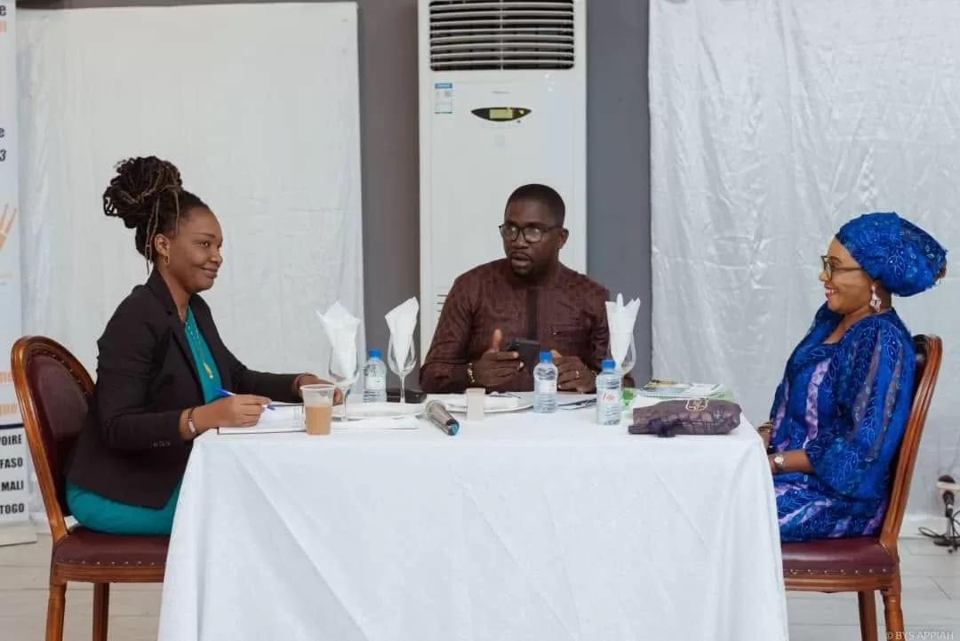Trois personnes échangent autour d’une table blanche dans une salle avec un climatiseur mural