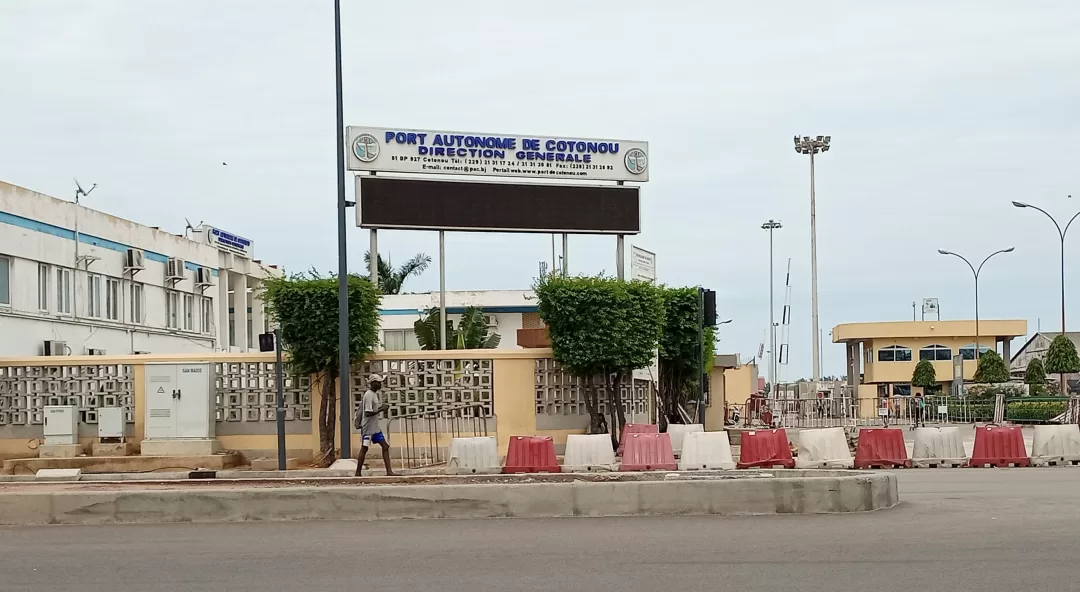 Entrée d'un bâtiment administratif avec un panneau Port Autonome de Cotonou Direction Générale et des barrières de chantier rouges et blanches.