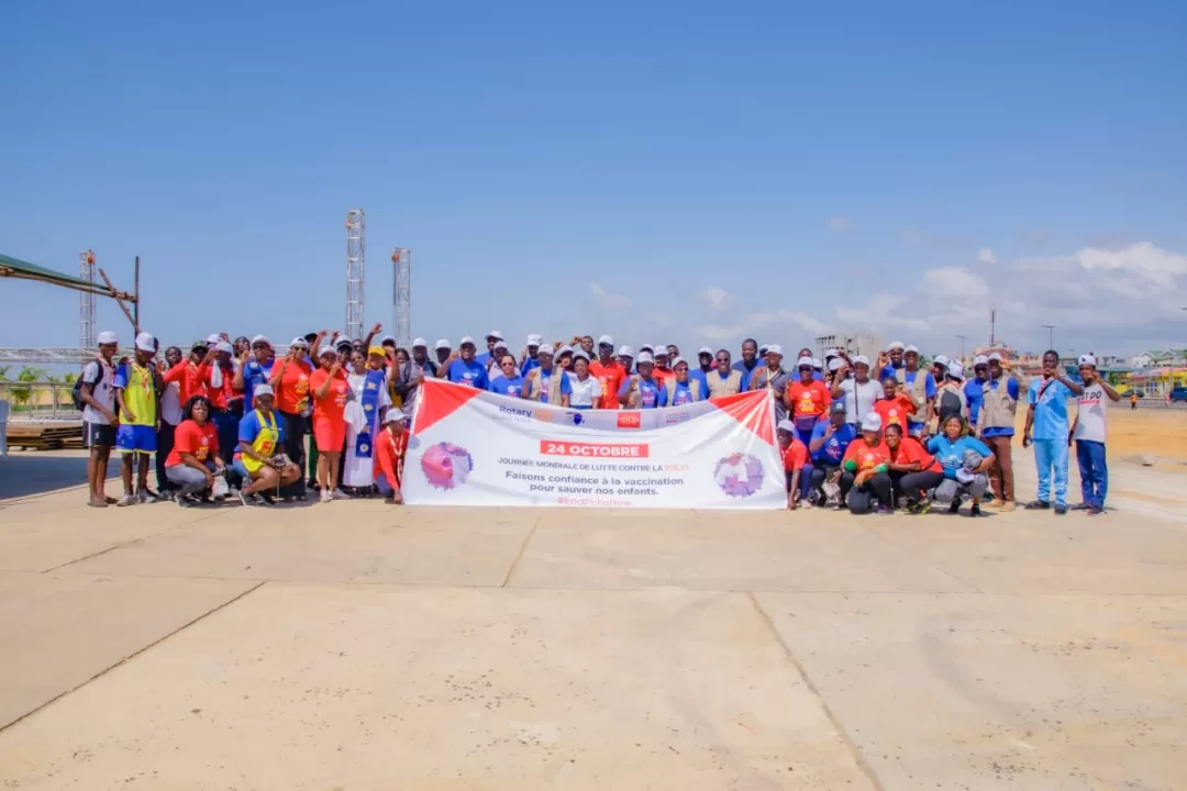 Groupe de personnes posant sur un terrain dégagé derrière une grande banderole blanche et rouge sous un ciel bleu avec quelques nuages.