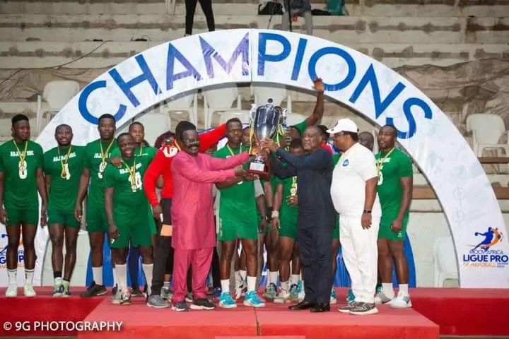 Joueurs en tenue verte fêtant la victoire avec un trophée devant une arche blanche marquée « CHAMPIONS
