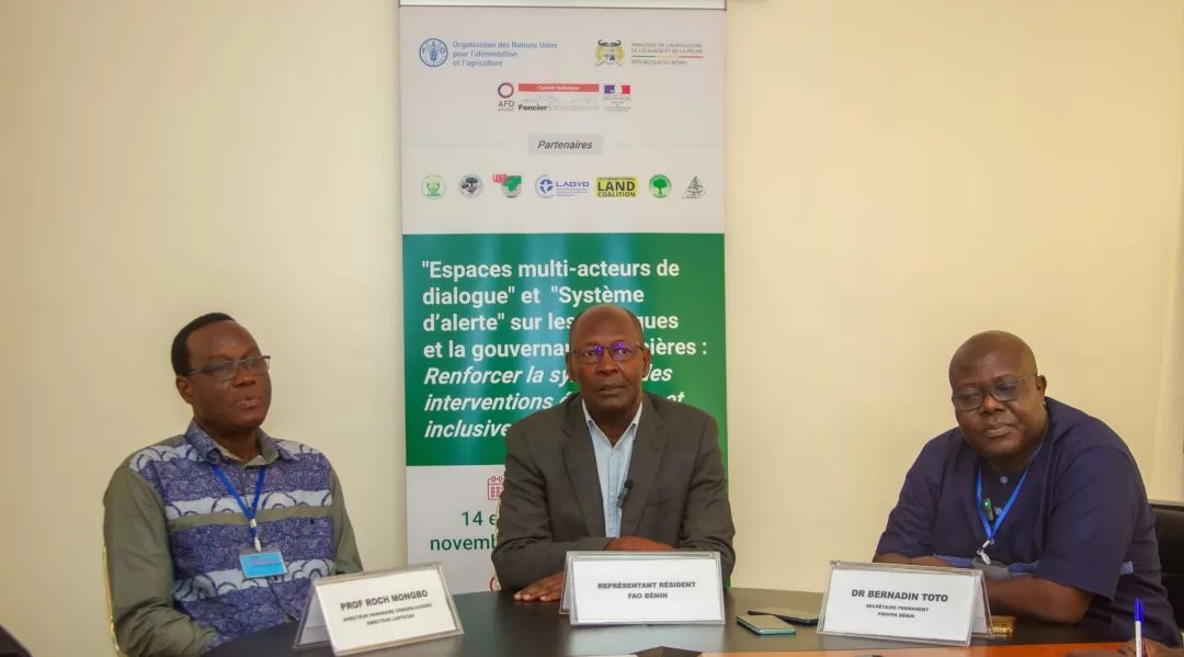 Trois hommes assis autour d'une table devant une affiche portant un texte sur la gouvernance foncière