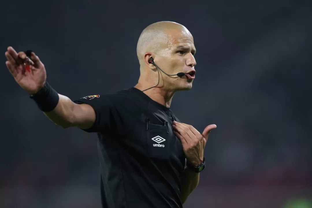 Arbitre en tenue noire avec micro et oreillette gesticule pendant un match de football