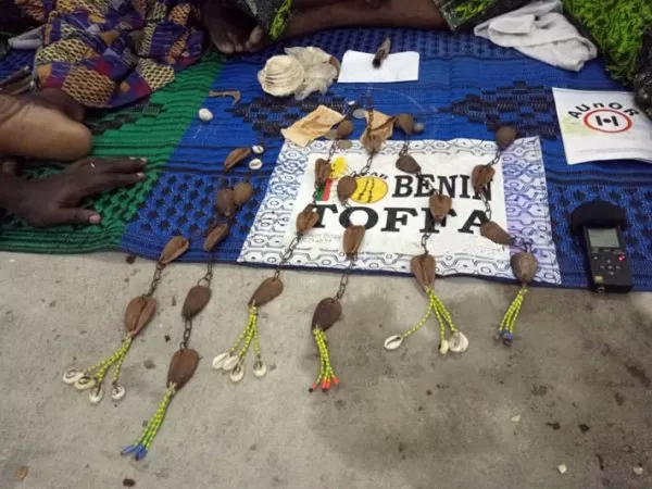 Objets artisanaux traditionnels posés sur une toile colorée près de mains et pieds visibles au sol