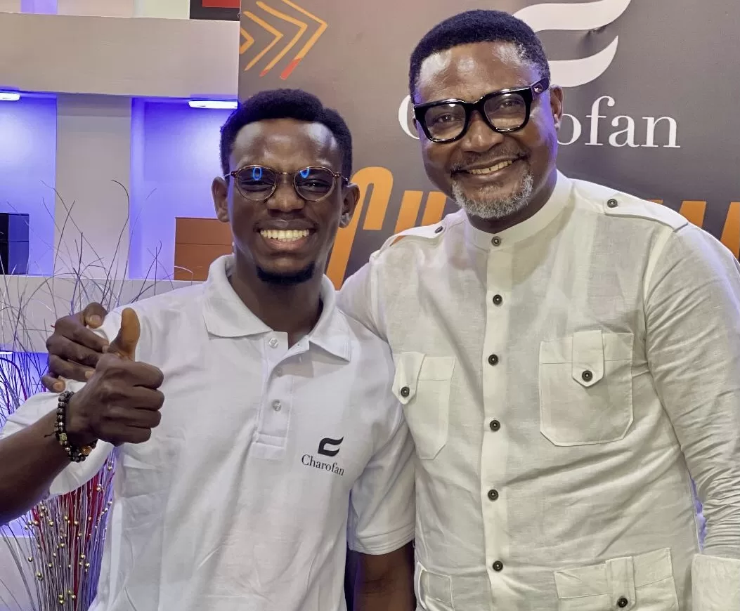 Deux hommes souriants portent des lunettes et des vêtements blancs avec un logo sur fond signalétique coloré
