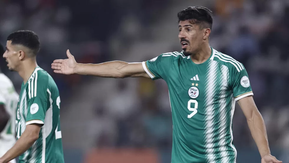 Deux joueurs en maillot vert discutent sur un terrain de football lors d'un match nocturne