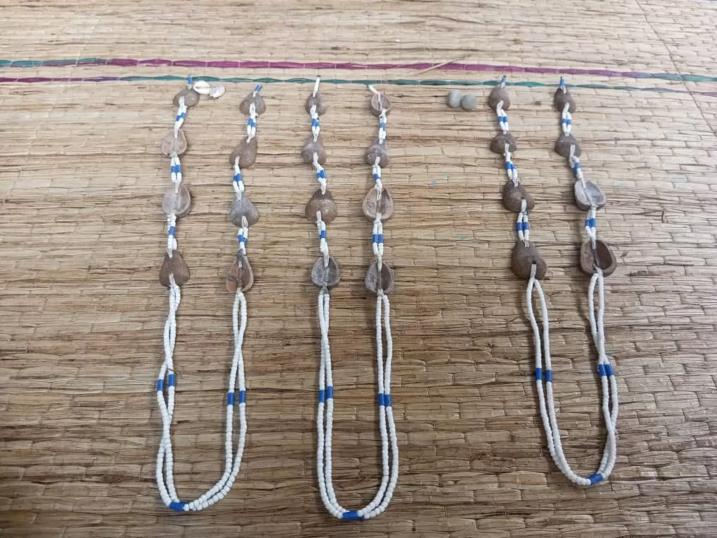 Quatre chaînes de perles blanches et bleues ornées de cauris posées sur un tapis en paille tressée