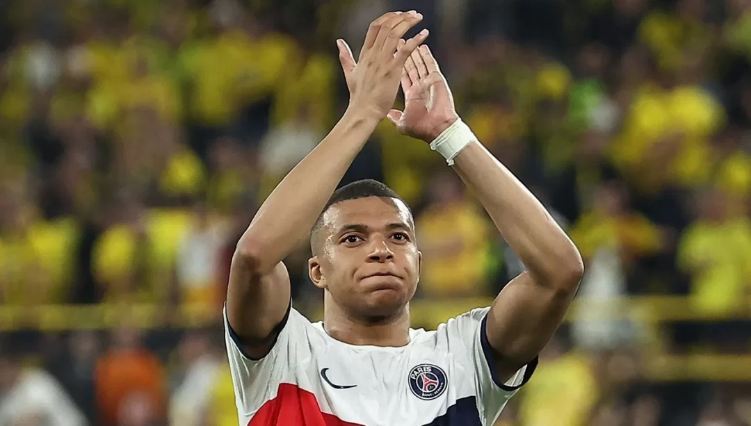 Un joueur de football applaudit avec les mains levées devant un public en tribunes floues dans un stade