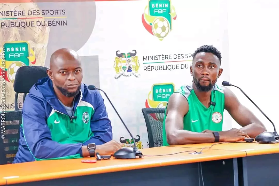 Deux hommes assis à une table de conférence avec microphones et logos sportifs en arrière-plan